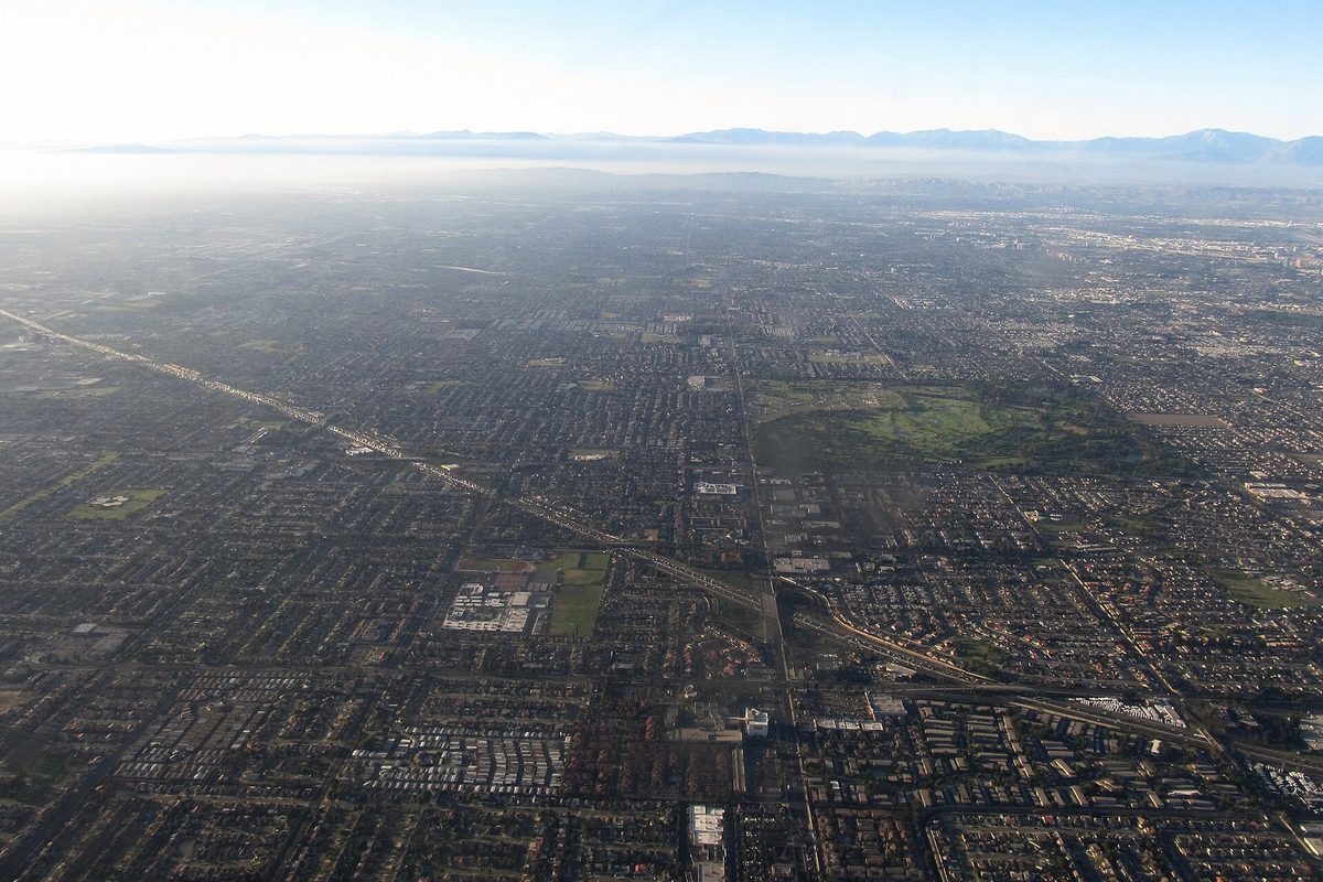 Aerial view of Interstate 405 cutting diagonally through the flat street grid of Fountain Valley and Westminster, with mountains on a hazy horizon