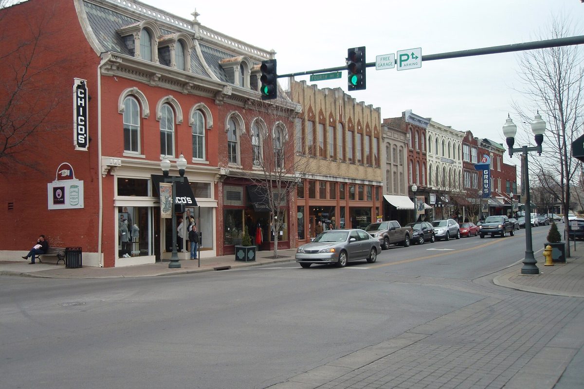 An ornate red-brick building on the corner of 4th Avenue and Main Street in downtown Franklin, with a traffic signal overhead and cars parked along the curb