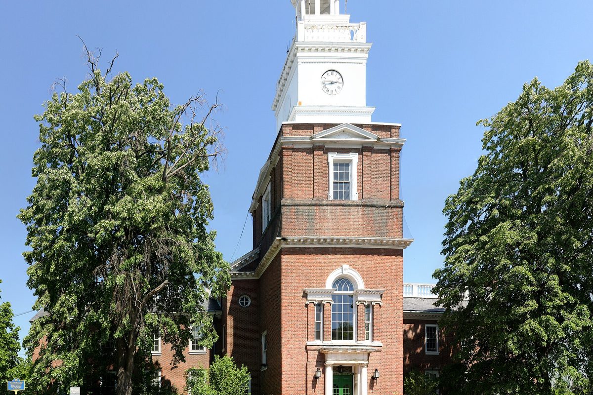 Freeport's red brick Village Hall with its white clock tower, framed by tall leafy trees under a clear blue sky