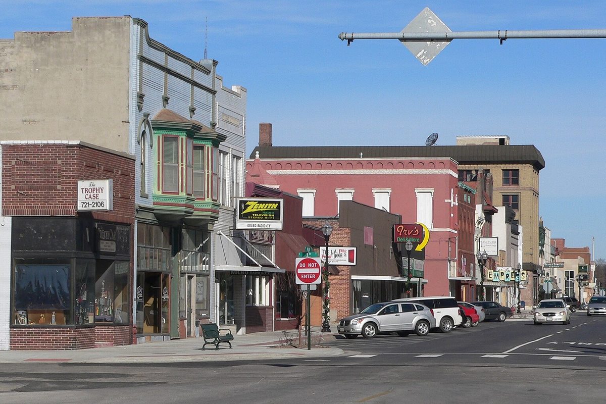 Downtown Fremont looking north up Main Street from 3rd Street, with old brick storefronts, a green bay-windowed building, a Zenith sign and cars parked at the curb under a blue sky