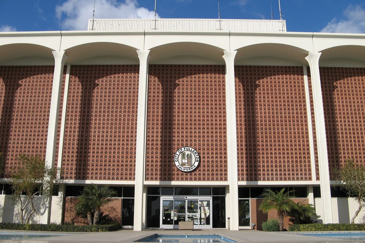 Fullerton City Hall on Commonwealth Avenue, a white arcade of tall arches over brick screen walls, with the city seal above glass doors and palms in front