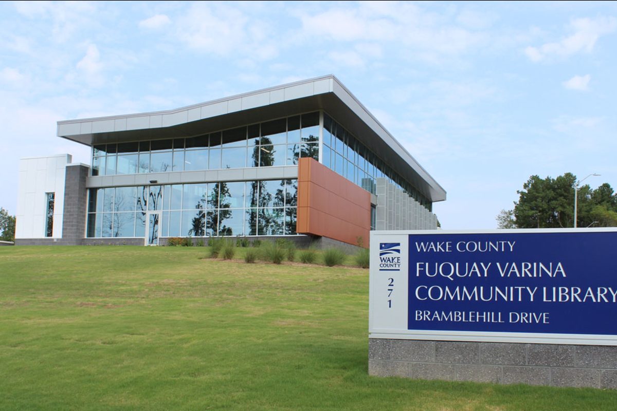 The modern glass-fronted Fuquay-Varina Community Library on Bramblehill Drive, with a blue Wake County sign on a grassy lawn