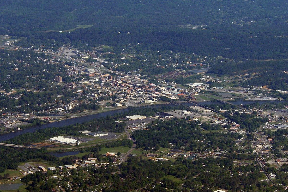 Aerial view of Gadsden, with the downtown blocks sitting beside a wide river and wooded hills rising all around the town