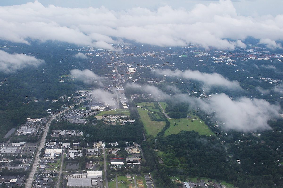 Aerial view of Gainesville under low clouds, with a long road running north through a thick tree canopy past open green fields