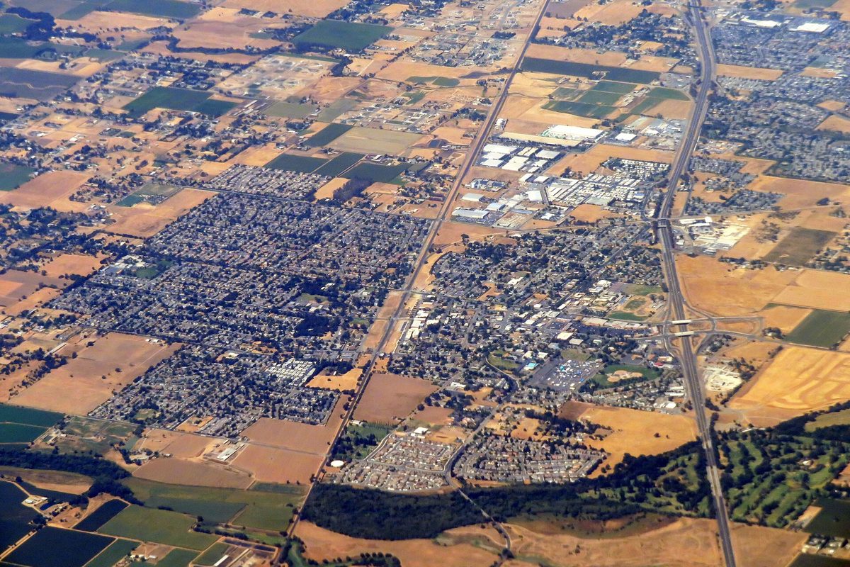 Aerial view of Galt's neighborhoods ringed by farm fields, with a rail line through the middle of town and a freeway along the right edge