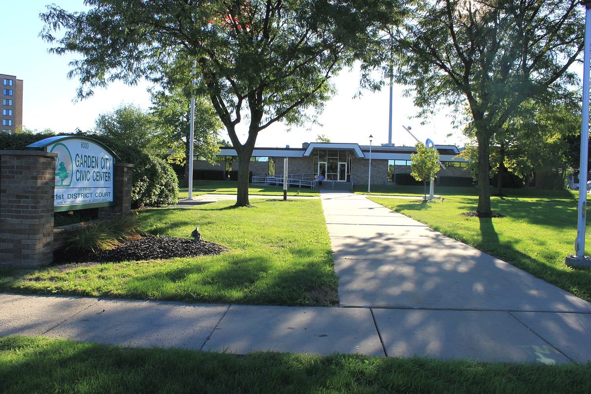 The Garden City Civic Center sign on a brick base in front of a low, flat-roofed building, with shade trees and a sunlit lawn