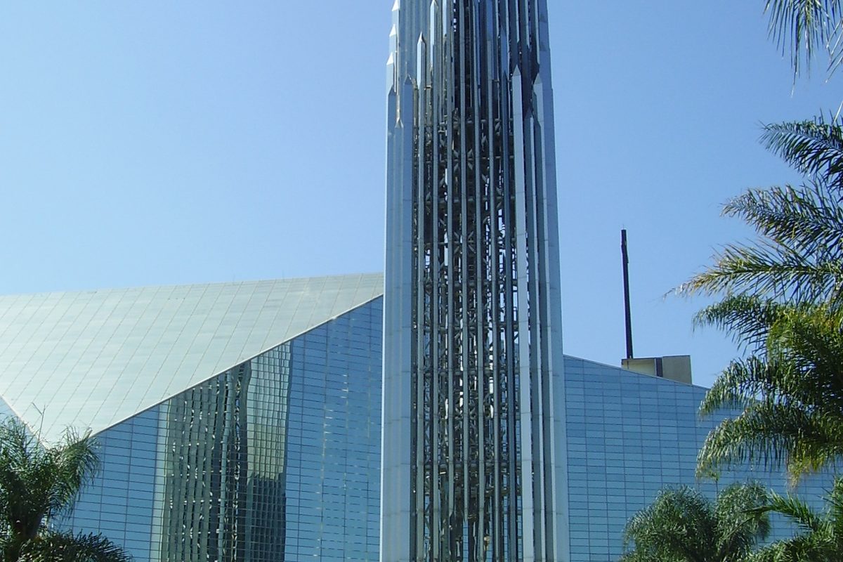 The mirrored glass bell tower and glass walls of Christ Cathedral in Garden Grove against a blue sky, framed by palm fronds
