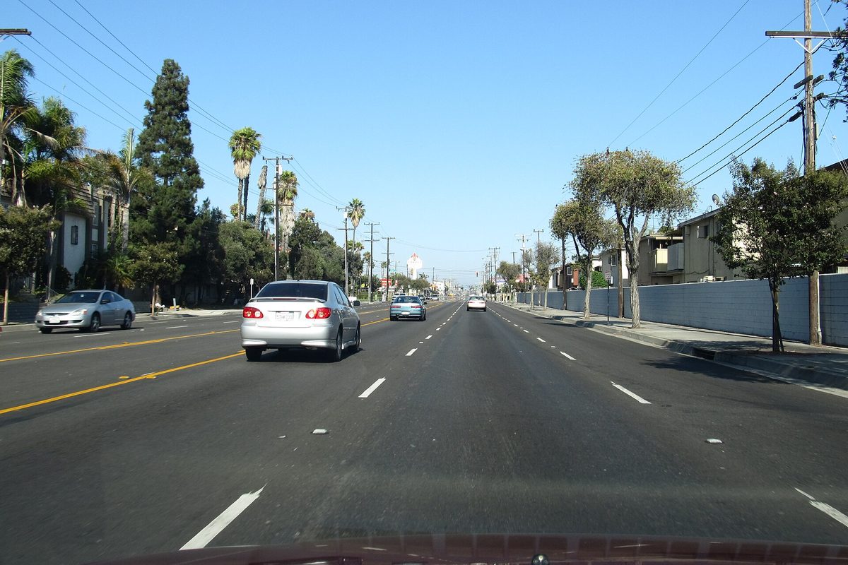 Rosecrans Avenue in Gardena seen from a moving car, with palm trees, apartment buildings and light traffic under a blue sky