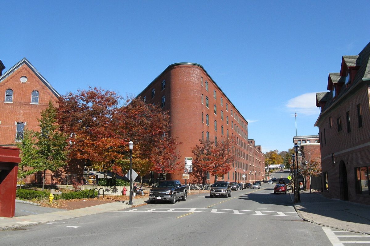 Central Street in Gardner on a clear autumn day, with a long curved brick mill building, red-leaved trees and parked pickup trucks