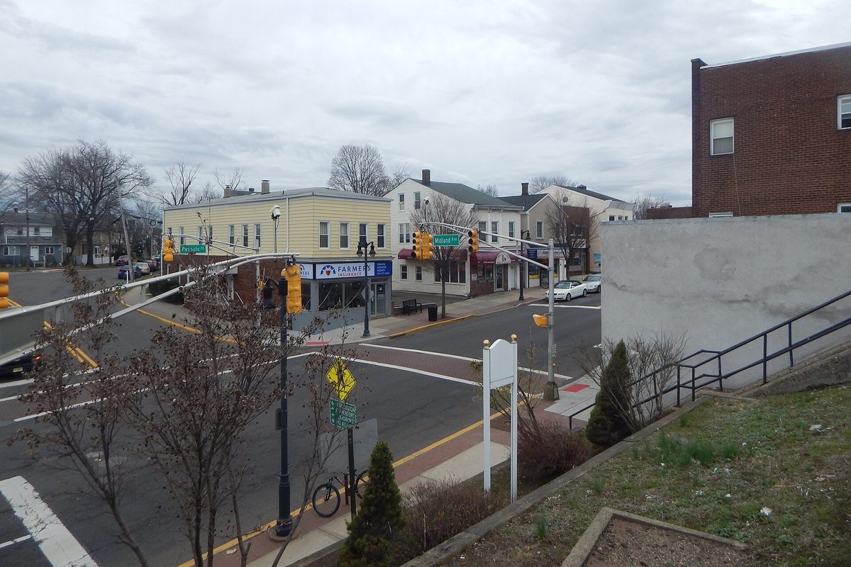 A street corner in Garfield with traffic lights, a crosswalk and a row of two-story shops and houses under an overcast sky