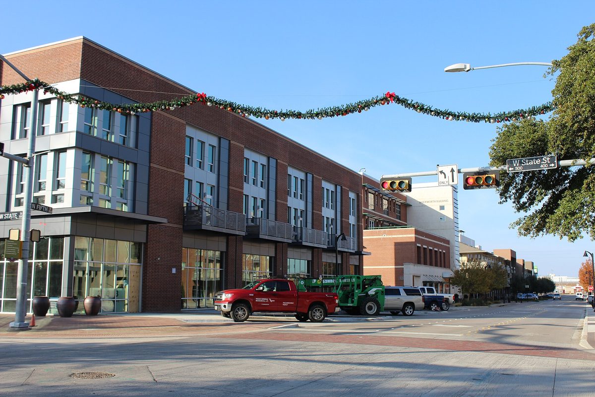 Holiday garland strung across a brick building at State Street and 5th Street in downtown Garland, with a red pickup stopped at the light