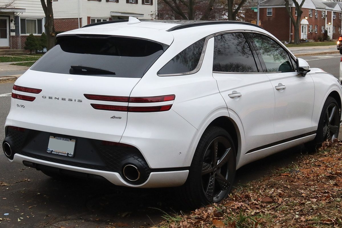 A white Genesis GV70 SUV seen from the rear corner, parked along a residential street