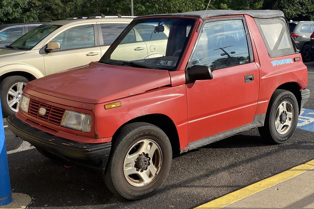 A red 1995 Geo Tracker LSi two-door convertible with a black soft top and a scuffed front bumper, parked in a lot