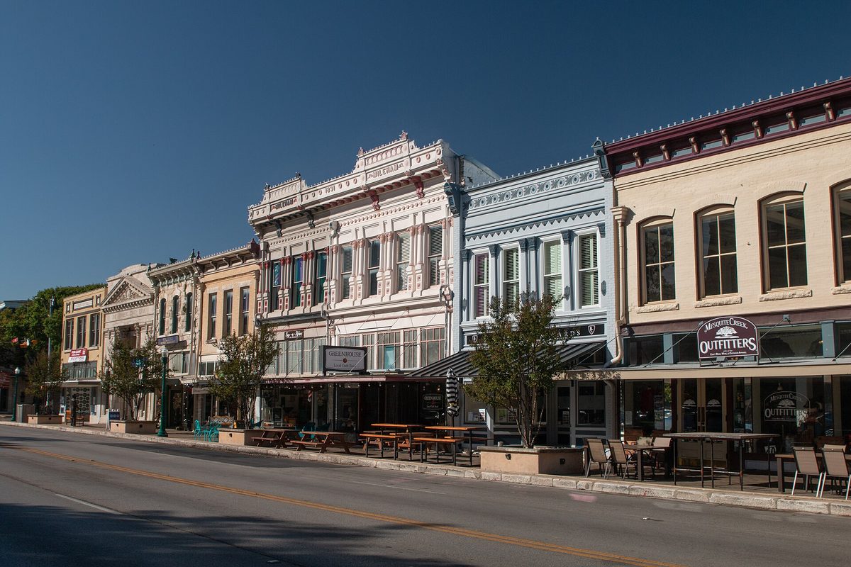 Ornate Victorian storefronts painted cream, blue and white along a sunny street in downtown Georgetown, with picnic tables and patio chairs on the sidewalk