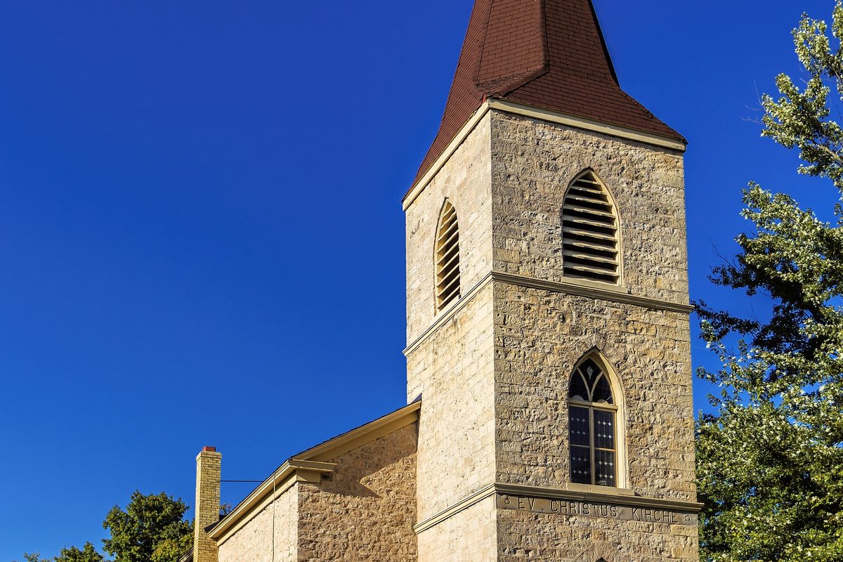 The cream stone bell tower of Christ Evangelical Church in Germantown, with louvered arched windows and a dark red steeple against a deep blue sky