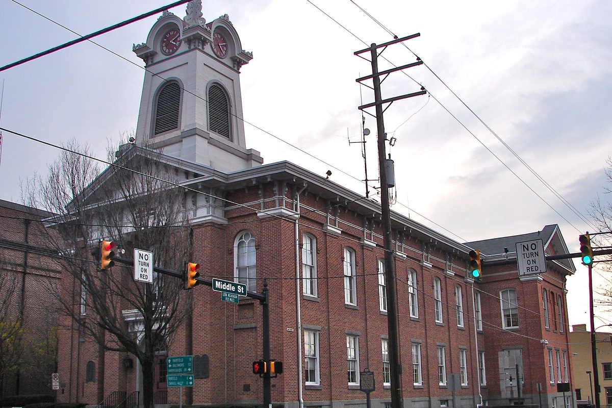 The red brick Adams County Courthouse in Gettysburg with its white clock tower, a Middle St sign, traffic lights and No Turn on Red signs on a cloudy day