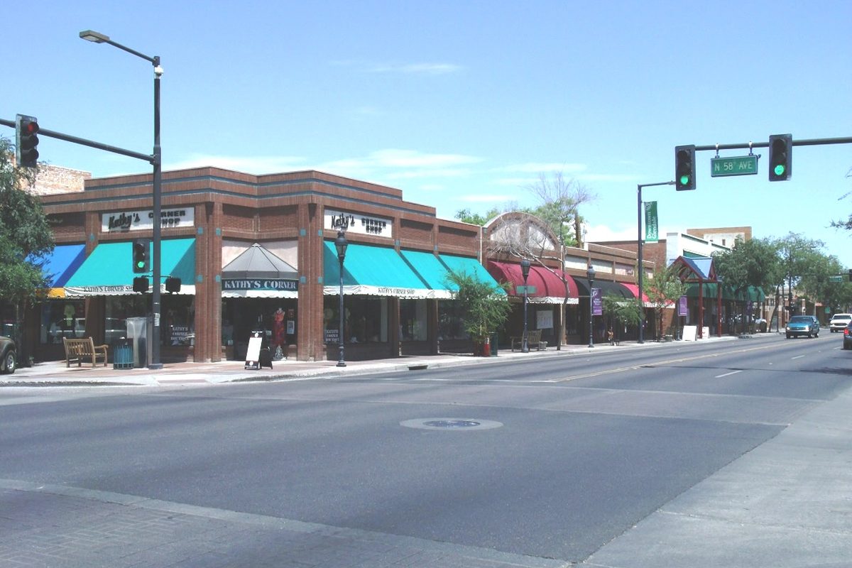 Low brick storefronts with teal and red awnings on Glendale Avenue at 58th Avenue in downtown Glendale, under a clear blue sky