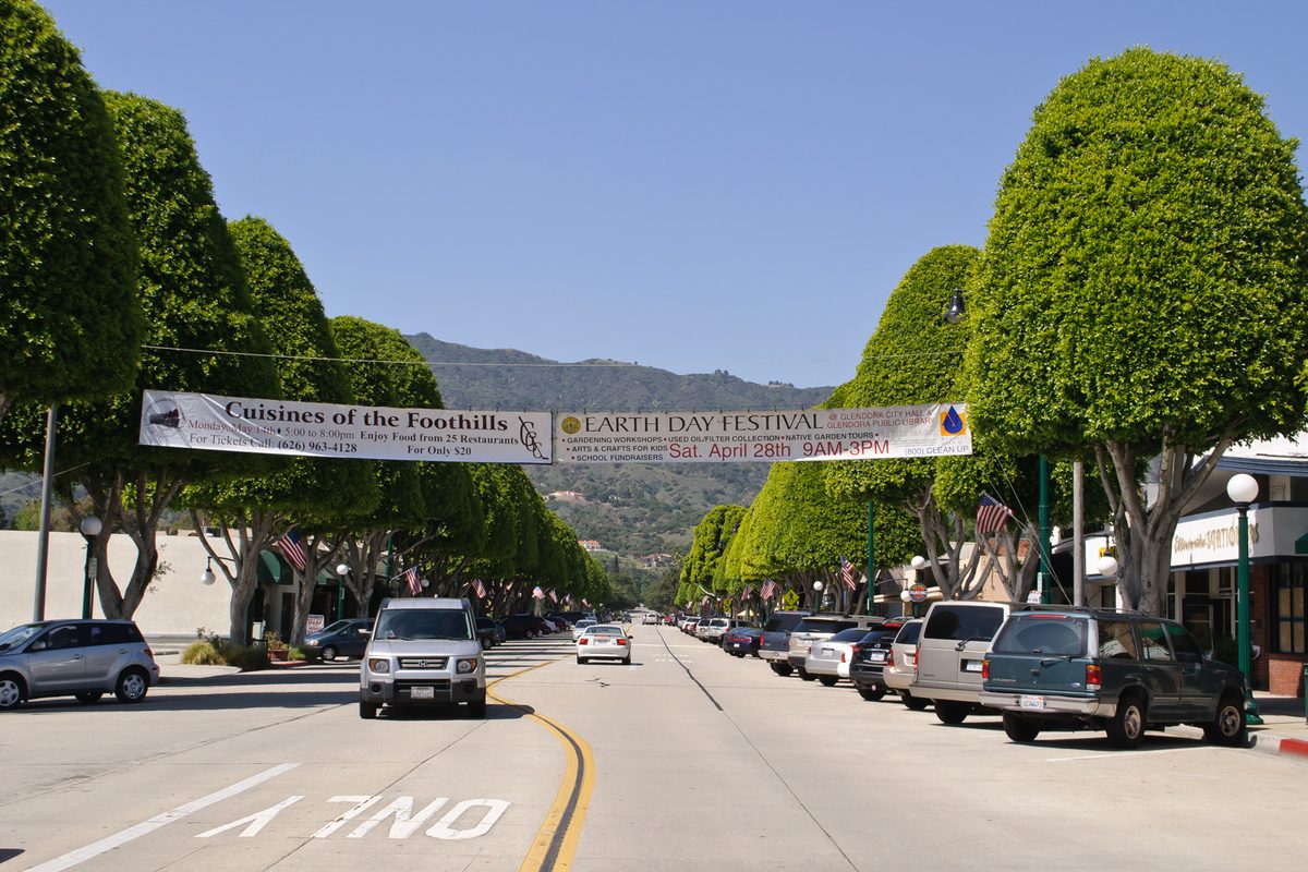 Glendora Avenue lined with round, clipped trees, with banners for Cuisines of the Foothills and an Earth Day festival strung across the street and the foothills behind