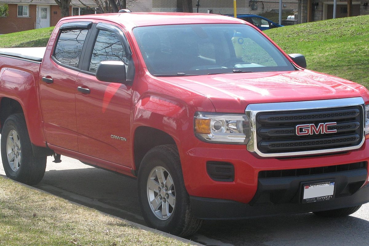 A red GMC Canyon crew cab pickup parked at a curb on a residential street