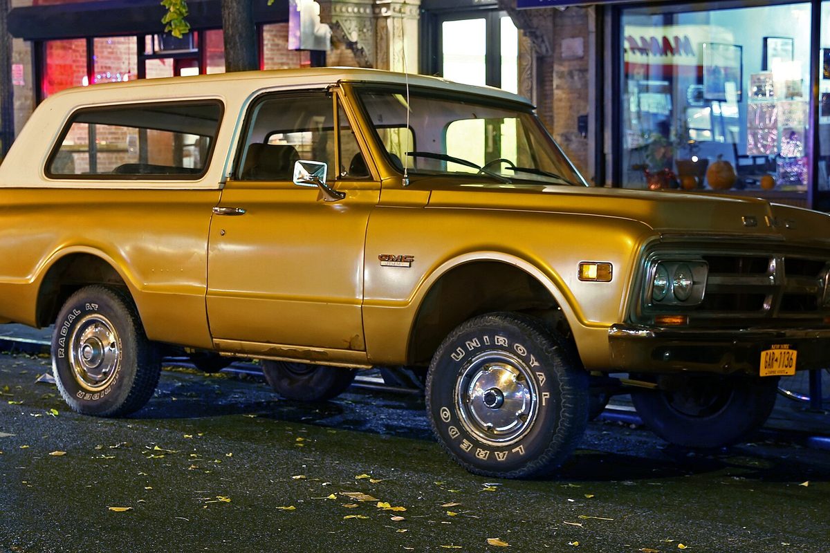 A gold early-1970s two-door GMC Jimmy K5 with a white hardtop, parked on a city street at night