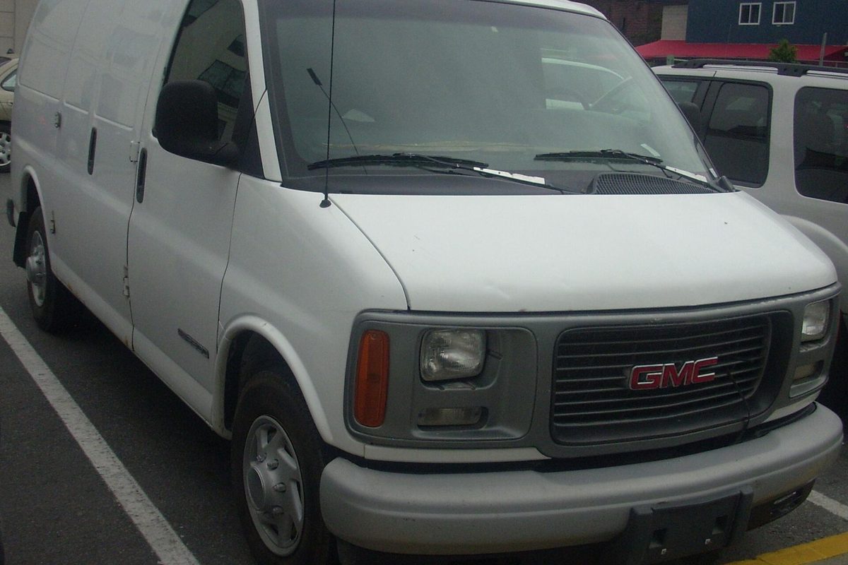 A white 1996-2002 GMC Savana van with a red GMC grille badge, parked in a lot