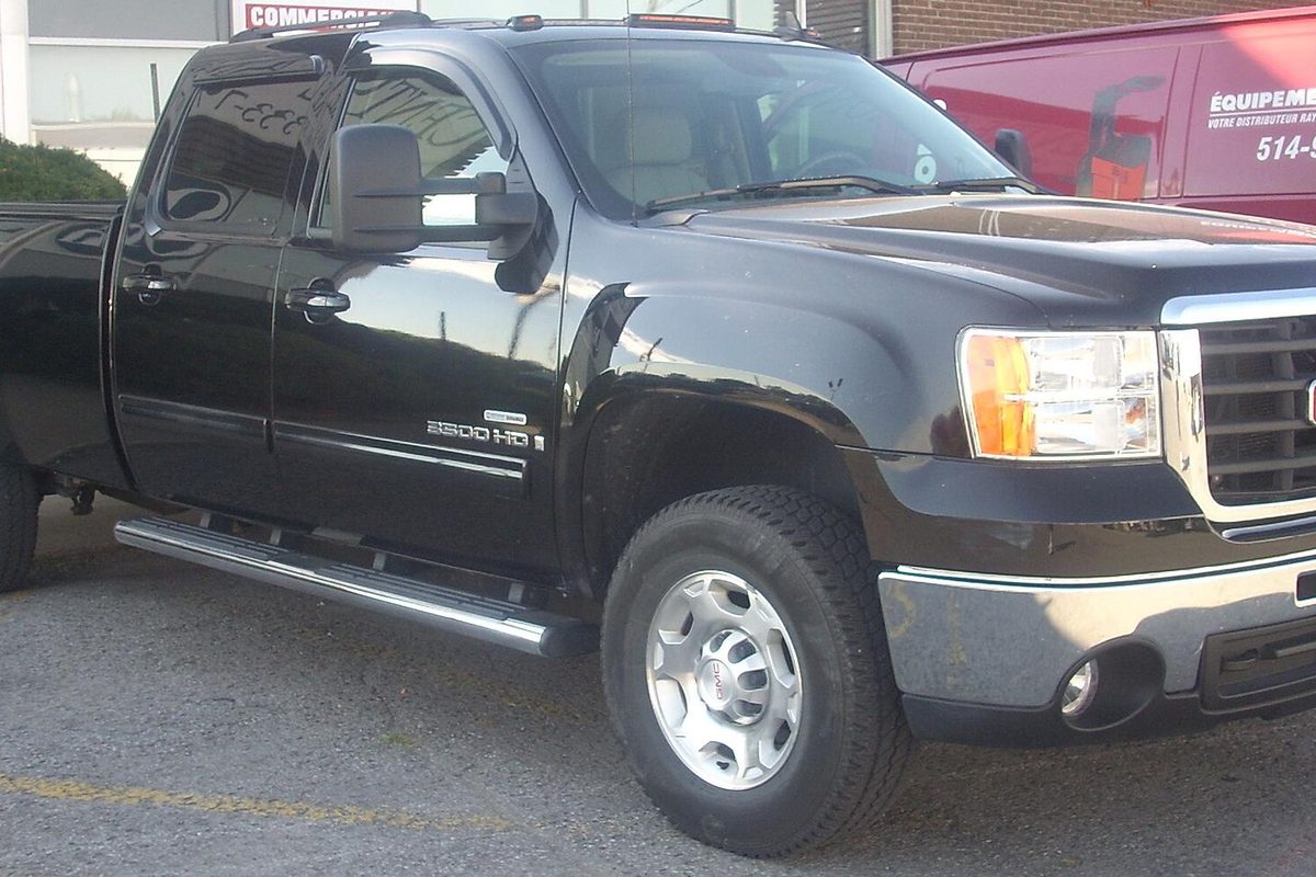A black GMC Sierra 2500HD crew cab pickup with chrome step bars, parked in a lot beside a red van