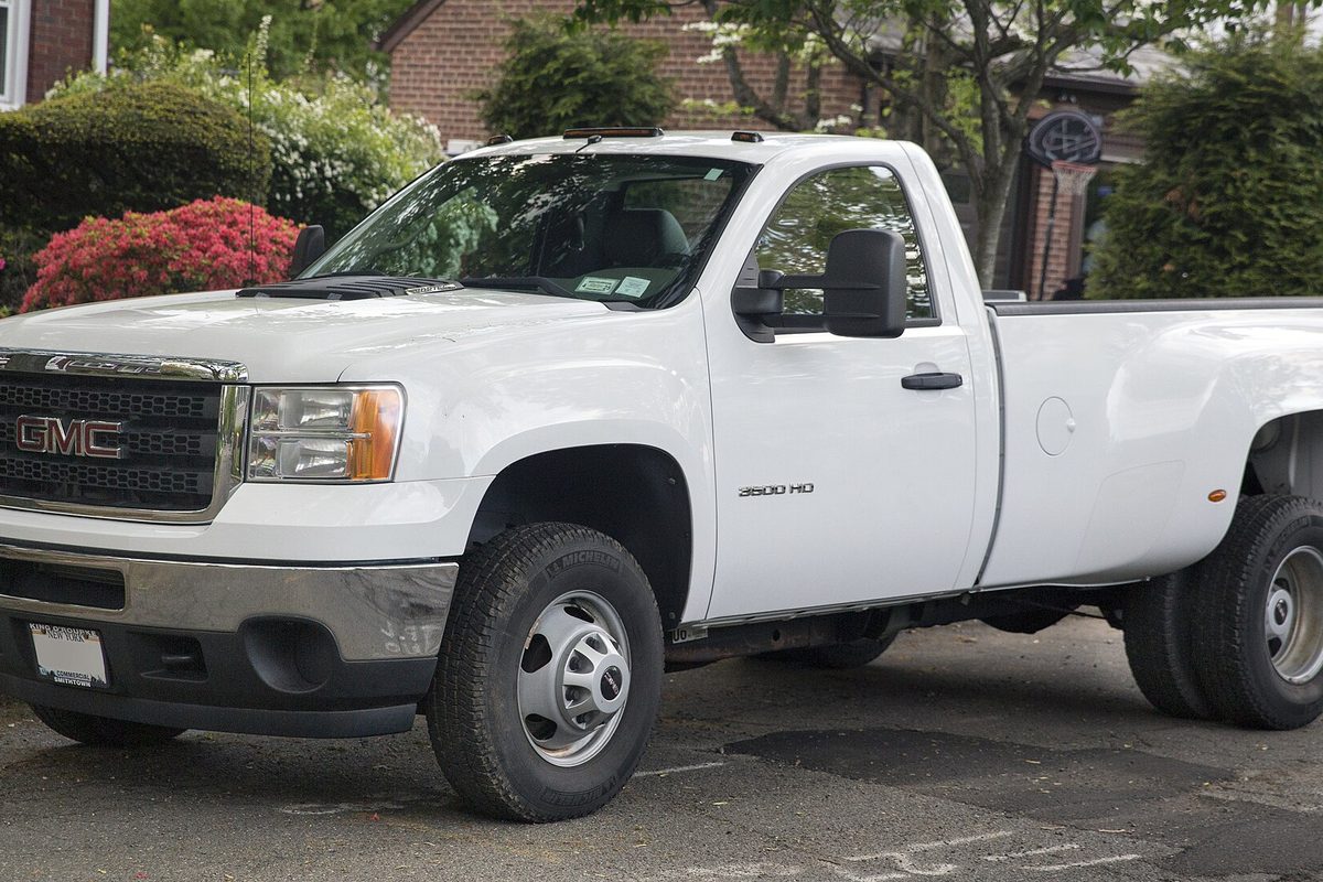 A white GMC Sierra 3500HD regular-cab dually work truck with tow mirrors and a long bed, parked on a residential street