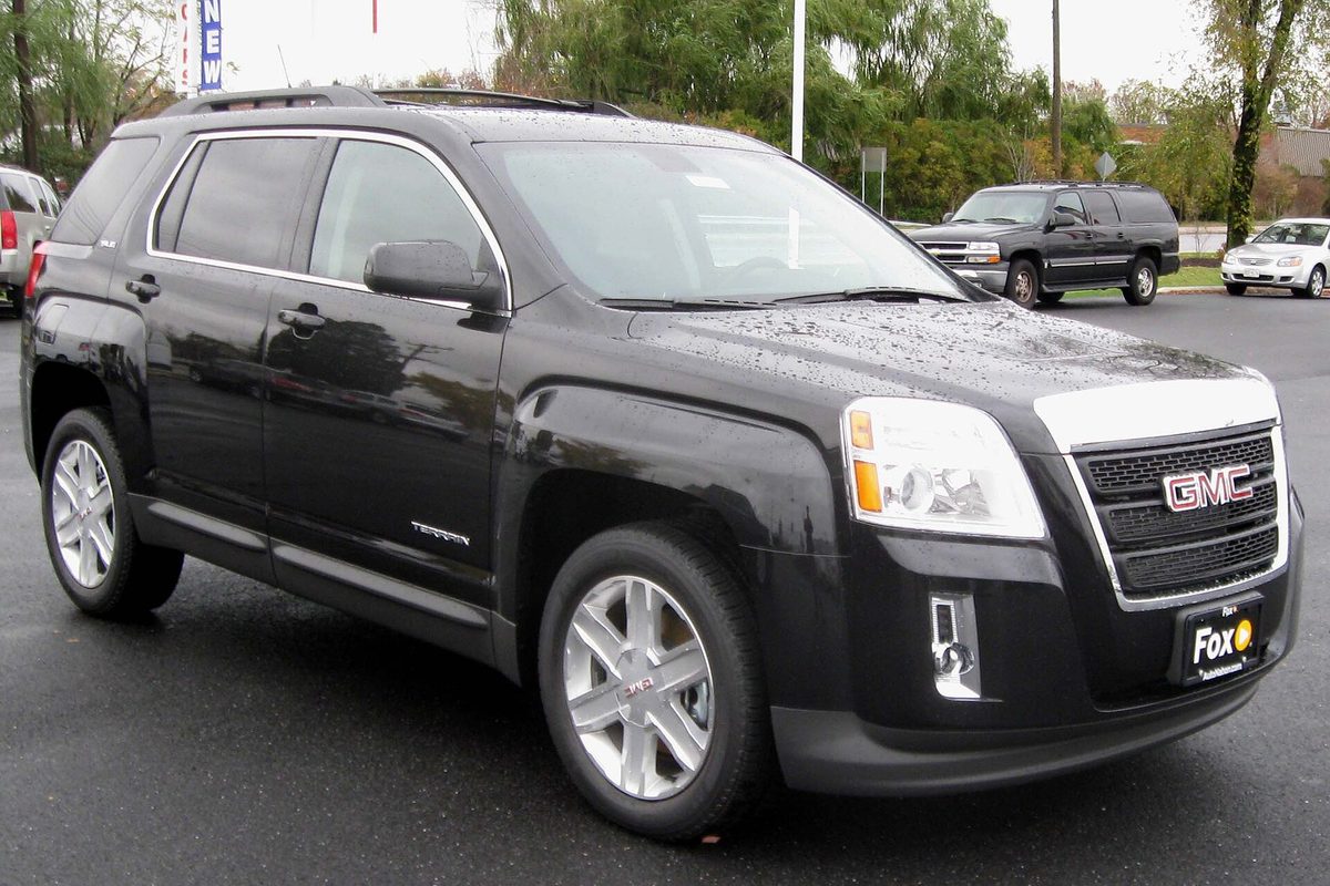 A black first-generation GMC Terrain with rain on the hood, parked on a wet dealer lot