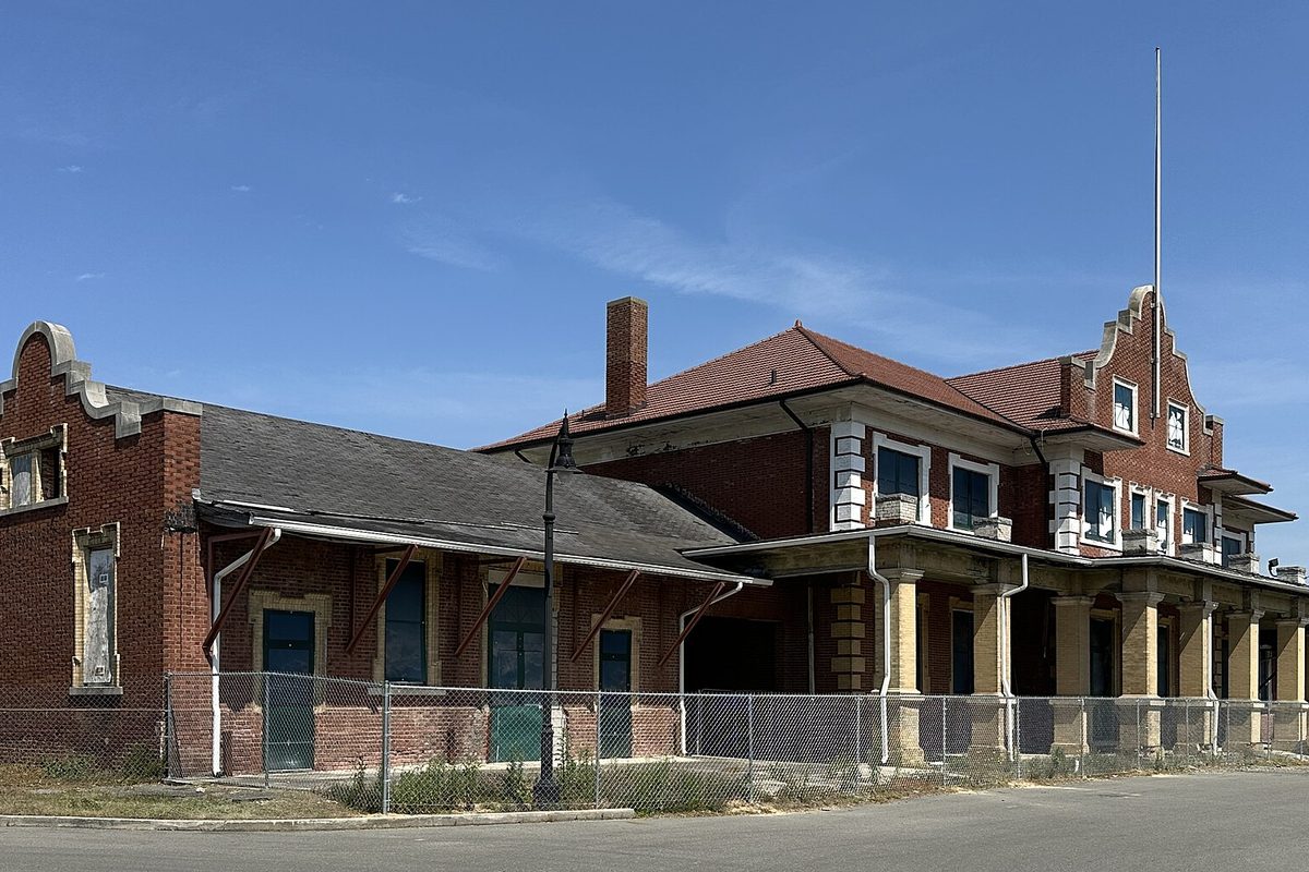 Goldsboro Union Station, a red-brick depot with curved gables and a tiled roof, behind a chain-link fence under a clear blue sky