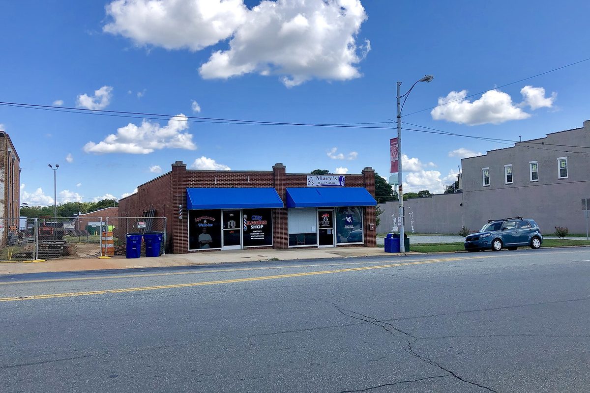 One-story brick storefronts with blue awnings on Court Square in Graham, a blue SUV parked at the curb under a bright sky