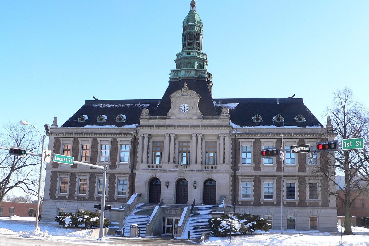 The Hall County Courthouse in Grand Island, a stone building with a green copper clock tower, snow on its front steps and a Locust St sign at the corner