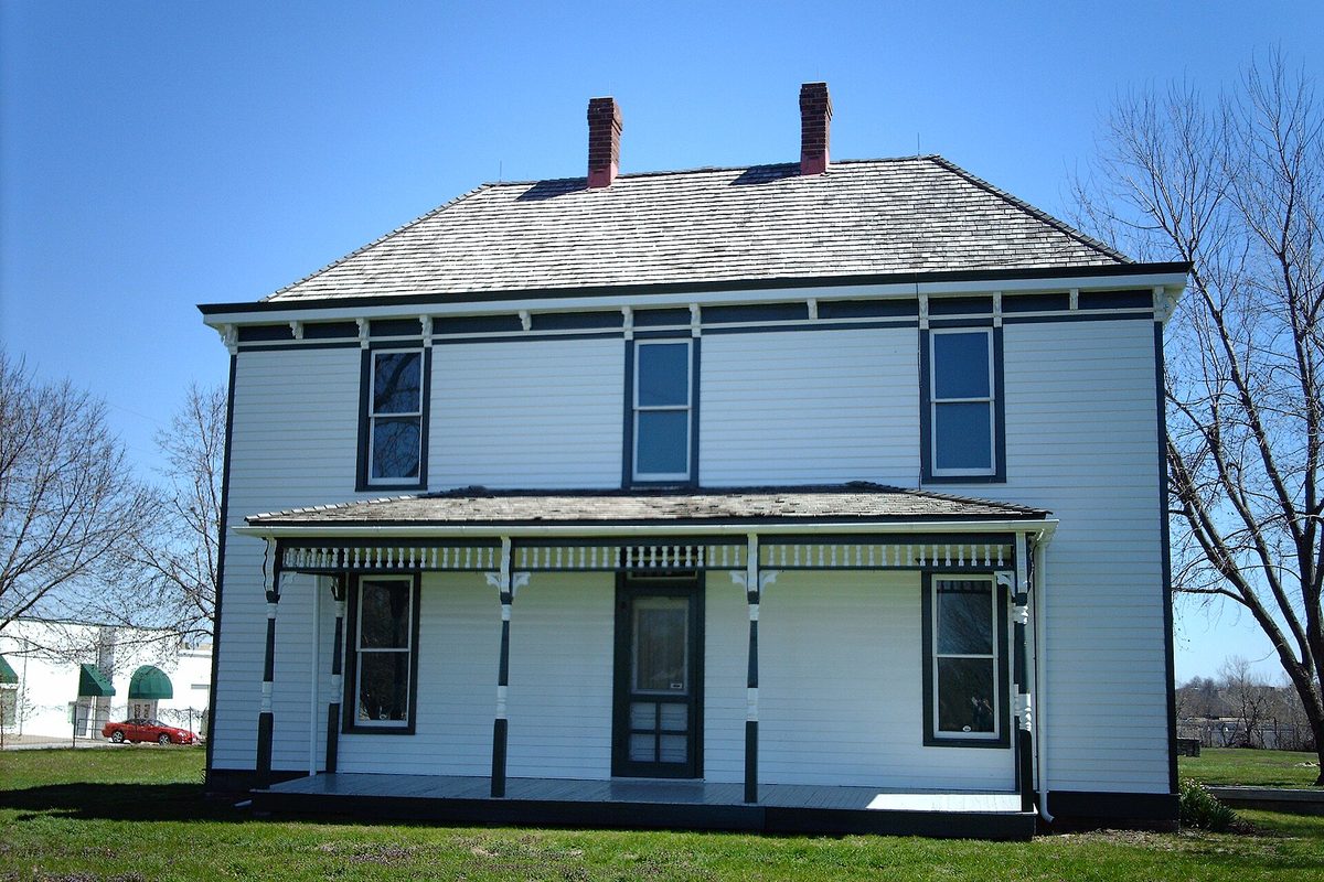 The white two-story Truman farm home in Grandview, with dark green trim, a full-width front porch and two brick chimneys