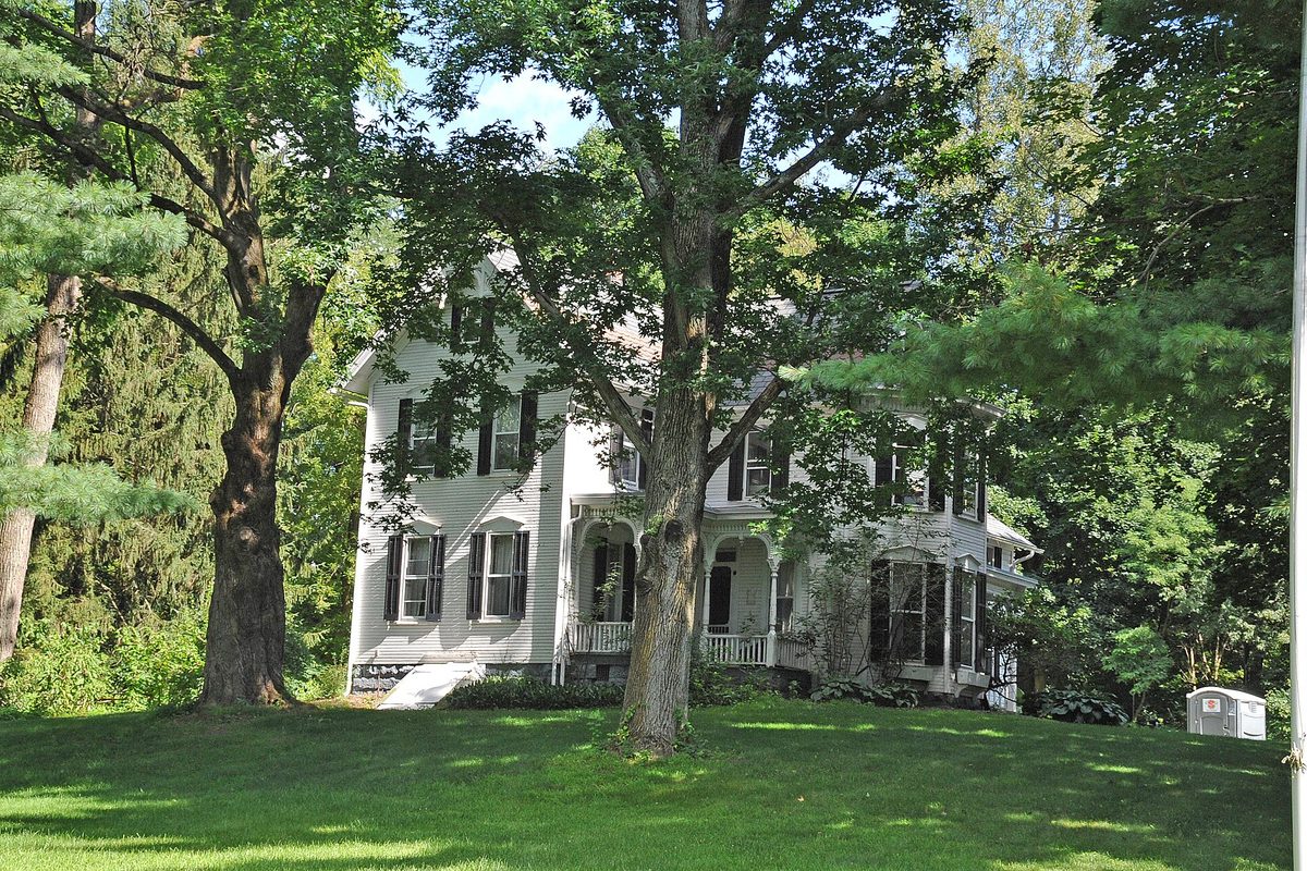 The Levi J. Hartong House in Green, a white two-story Victorian farmhouse with black shutters, set among tall trees on a wide lawn