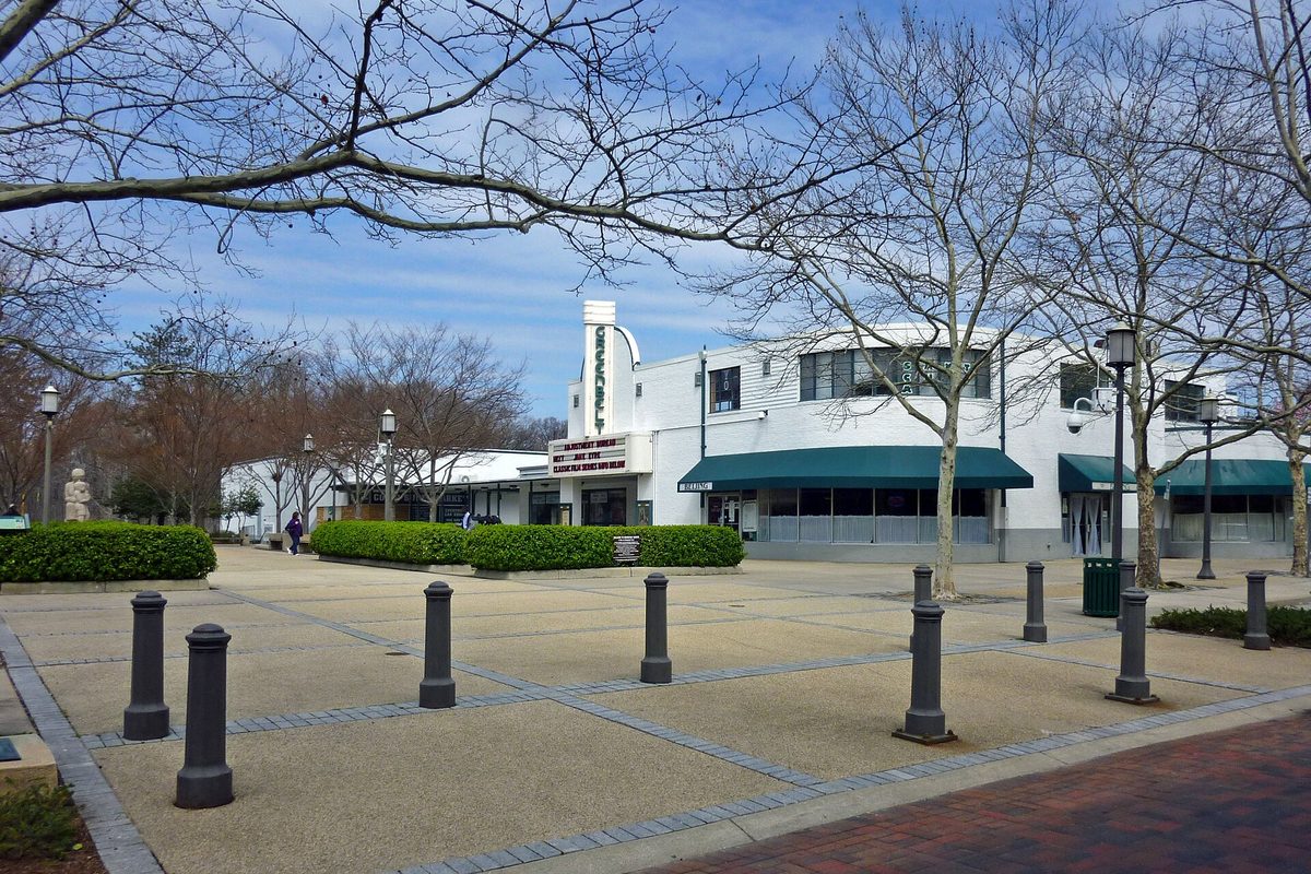 Roosevelt Center in Greenbelt: a white two-story building with green awnings and a vertical theater sign, behind a paved plaza lined with bollards and bare trees