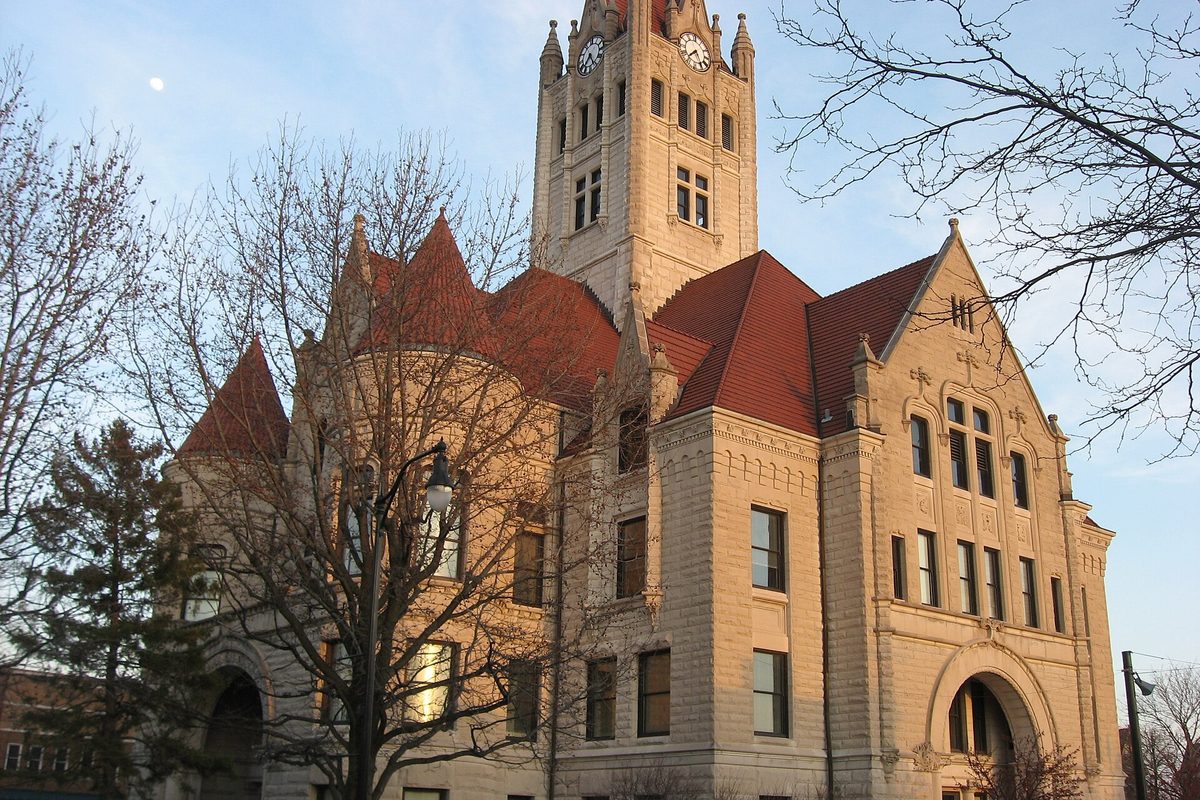 The stone Hancock County Courthouse in Greenfield, with red roofs, turrets and a clock tower, lit by low sun behind bare trees
