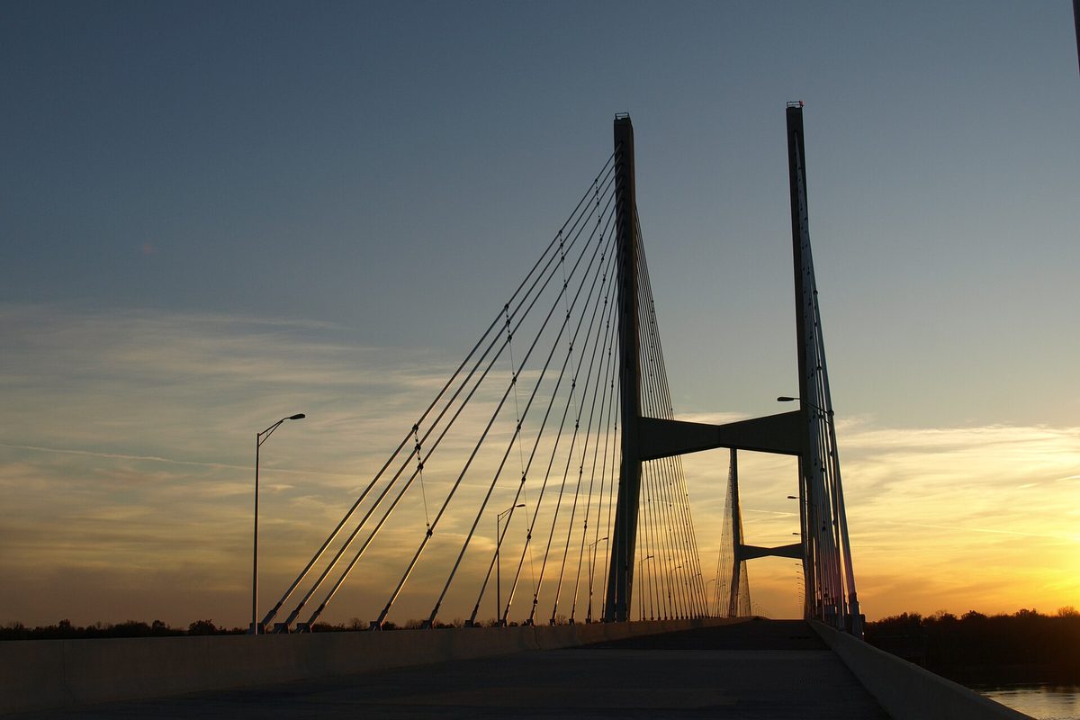 The towers and cables of the Greenville Bridge over the Mississippi River in silhouette against a sunset sky