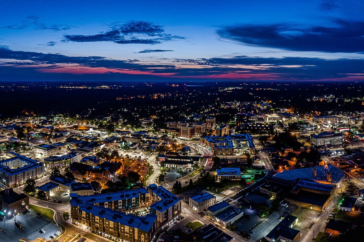 Aerial view of central Greenville at dusk, lit streets and apartment blocks under a pink and deep blue sky