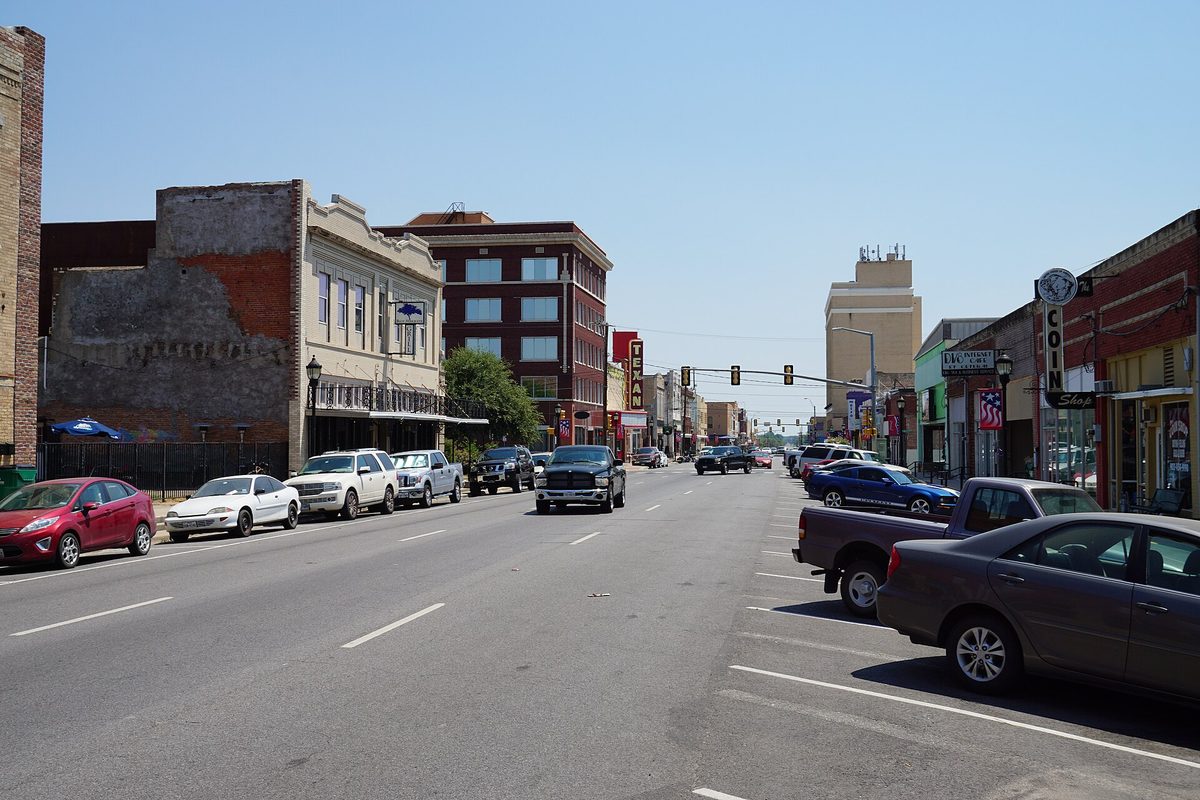 Lee Street in downtown Greenville, a wide street lined with old brick storefronts, a theater sign and parked cars and pickups under a clear sky