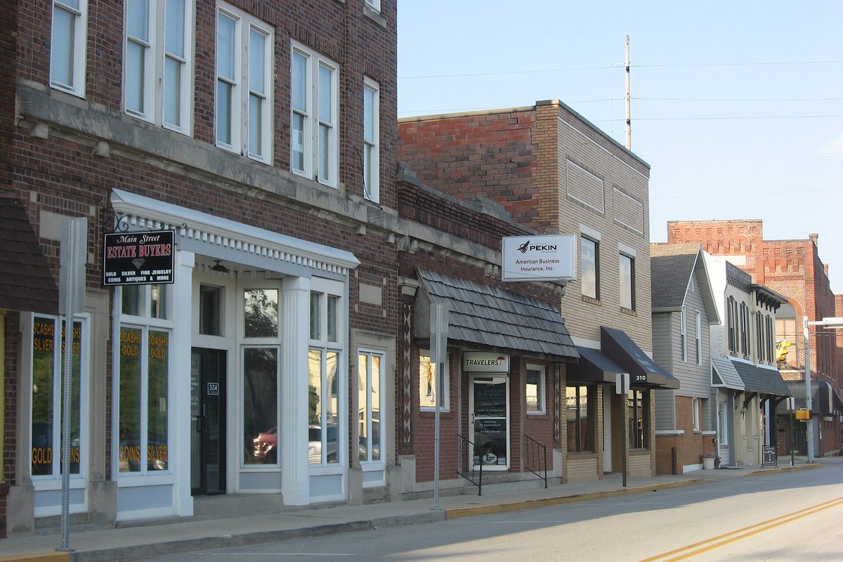 Two- and three-story brick storefronts on West Main Street in downtown Greenwood, one with a white-trimmed entrance, in late-day sun