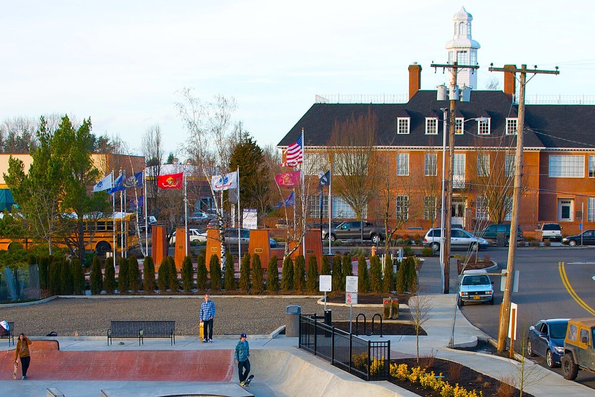 The skatepark in Main City Park, Gresham, with a row of flags and a brick building topped by a white cupola behind it