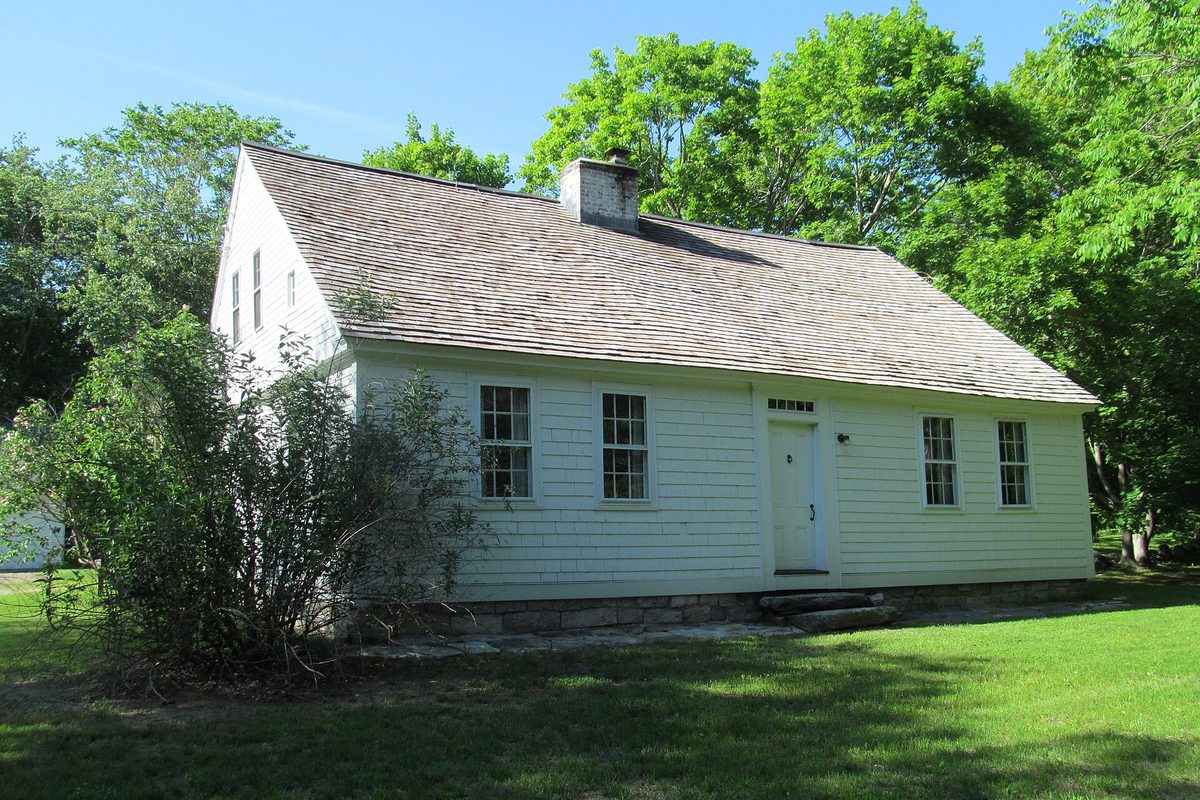 The Jabez Smith House in Groton, a white clapboard Cape with a weathered shingle roof and center chimney, on a green lawn below tall trees