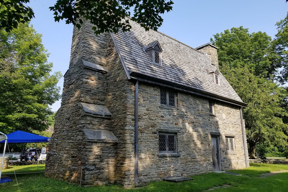 The Henry Whitfield House in Guilford, a stone house from about 1639 with a steep shingled roof and small leaded windows, among green trees
