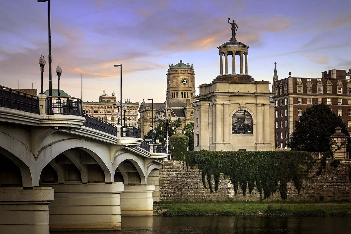 The Butler County Soldiers Monument with its statue on top, beside the arches of the High Street bridge over the Great Miami River in Hamilton at dusk