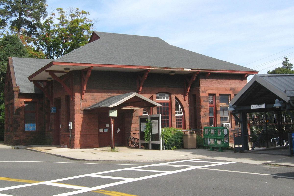The red stone Metro-North station house in Harrison with a broad gray roof and bracketed eaves, beside the platform shelter