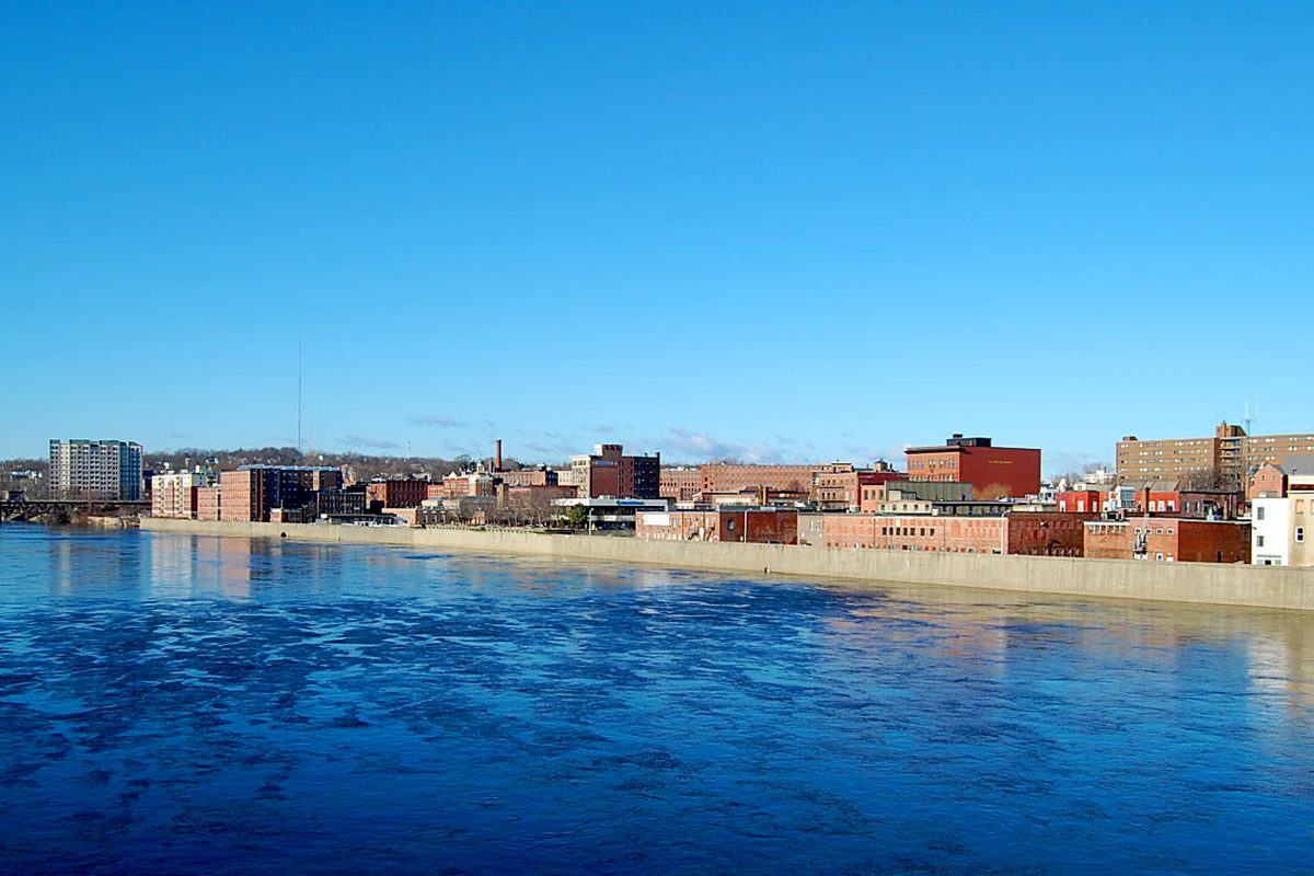 Haverhill's brick downtown buildings lining the Merrimack River under a bright blue winter sky, the water rippled by wind