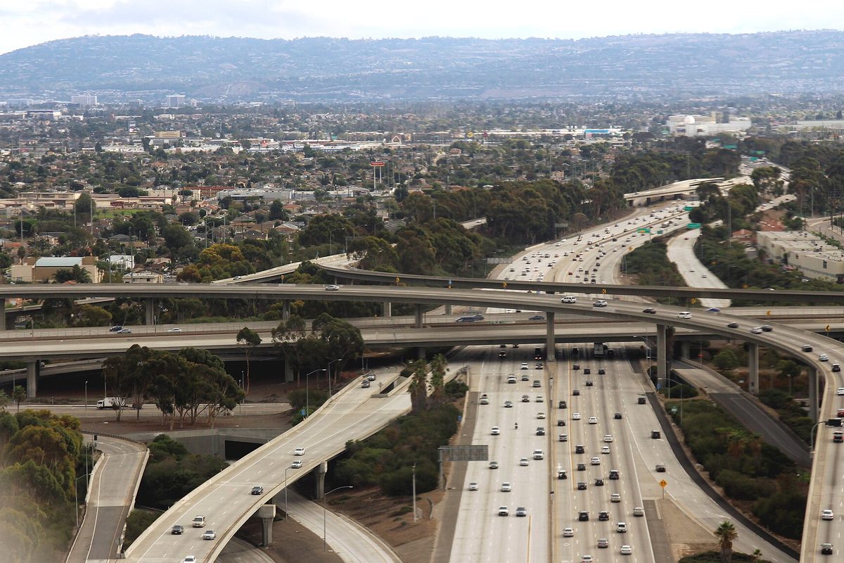 Aerial view of the 405 and 105 freeway interchange in the Hawthorne area, with traffic on the ramps, rooftops and hills in the distance