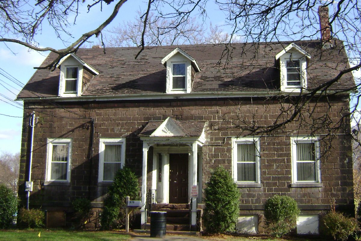The John W. Rea House in Hawthorne, a two-story brown stone house with three white dormers and a white front portico, seen through bare tree branches