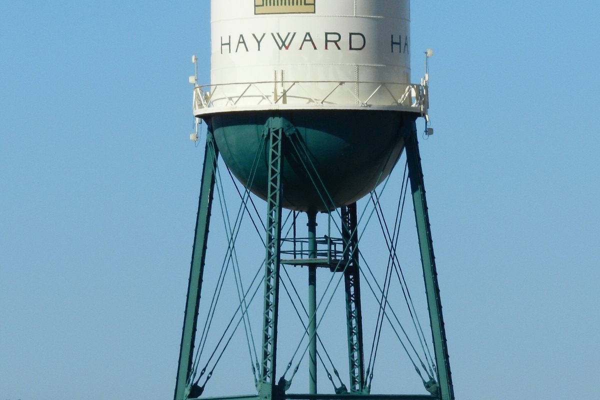 Hayward's white and green water tower on steel legs, its tank lettered HAYWARD, against a clear blue sky