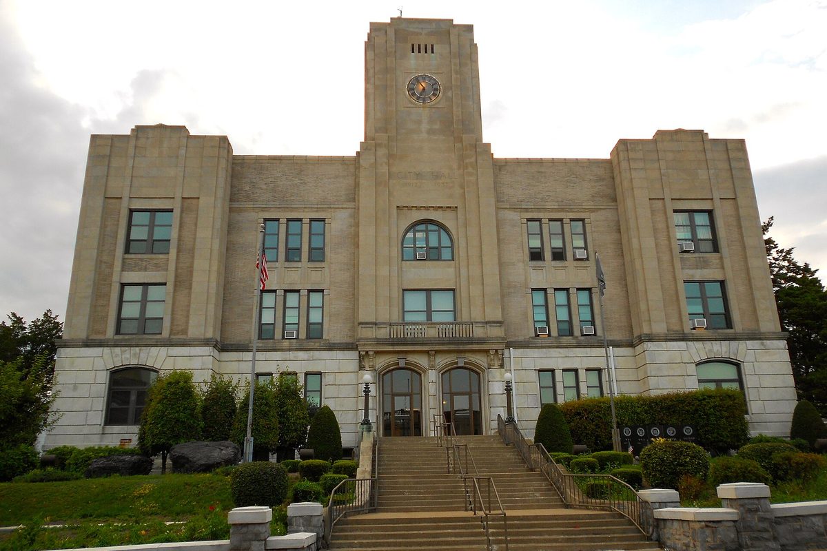 Hazleton's pale stone municipal hall with a clock in its central tower, arched doors and a wide flight of front steps lined with shrubs