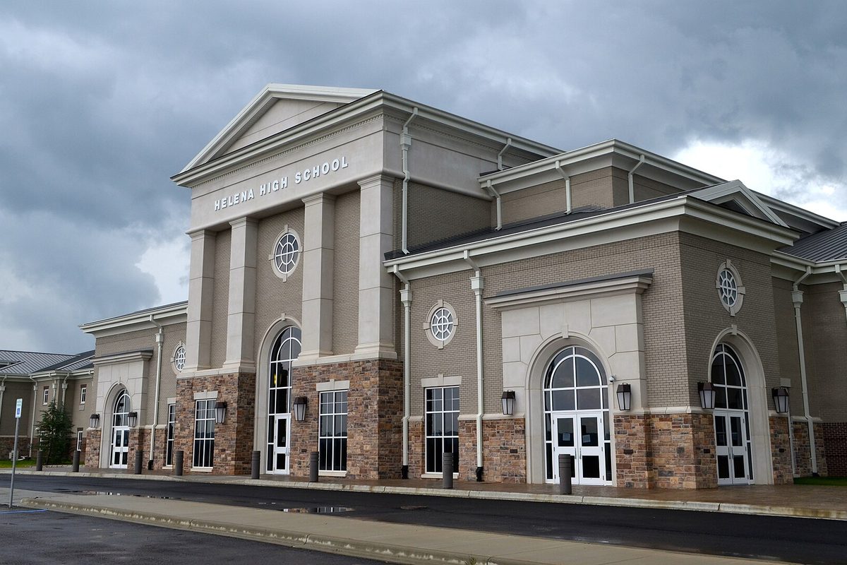 Helena High School's columned stone-and-brick entrance with arched windows and a gabled roof, under dark storm clouds